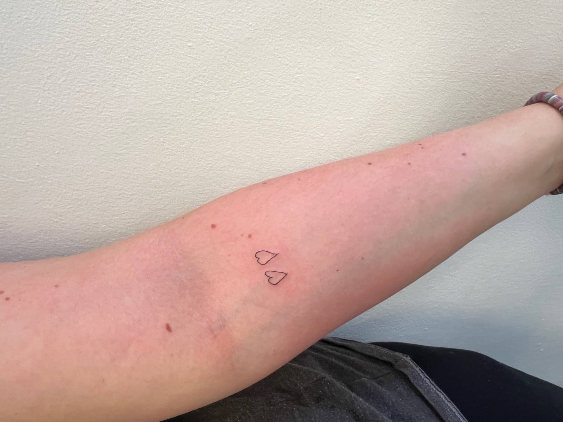 Two small heart outline tattoos on the forearm