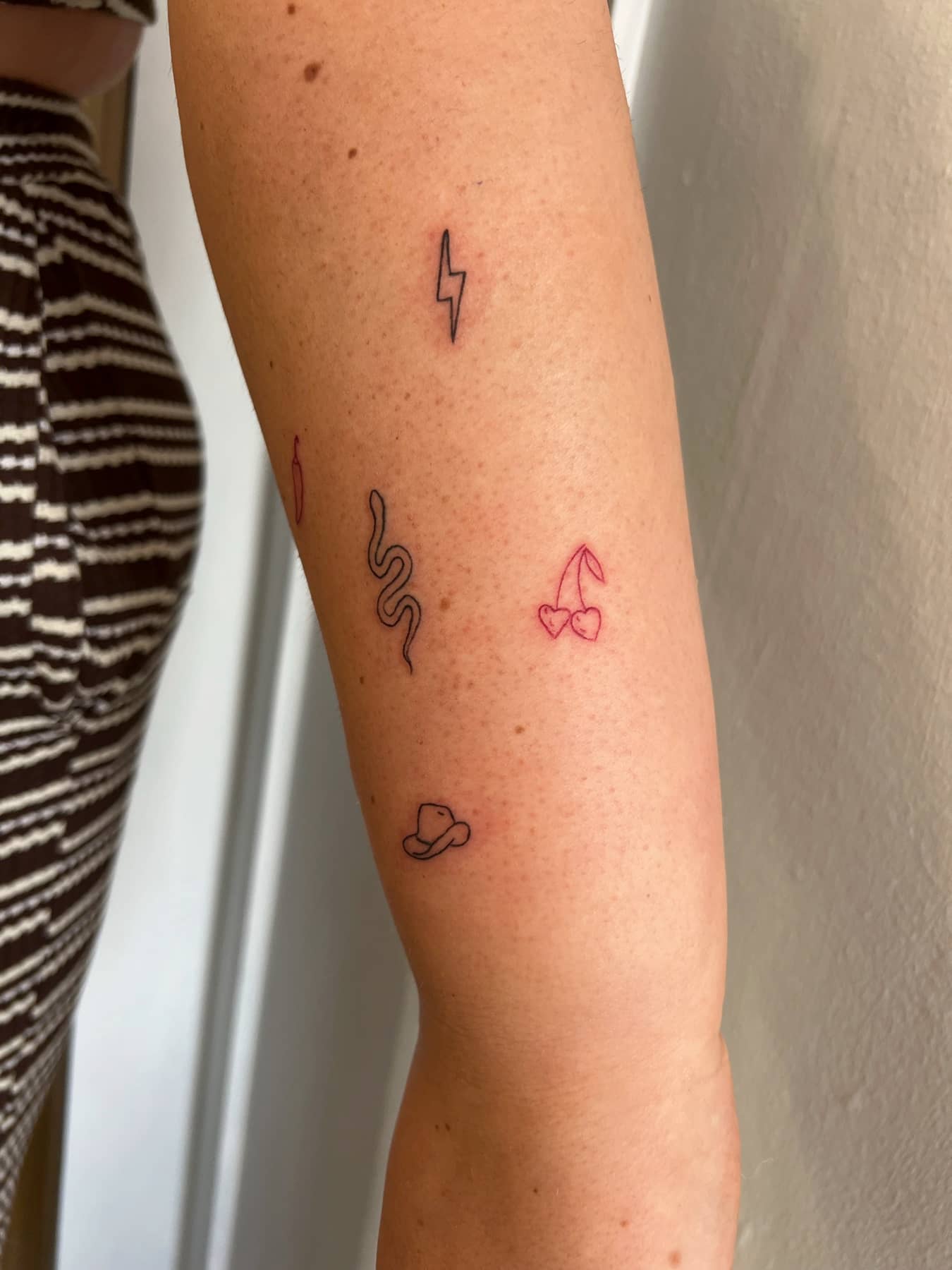 Fine line mini flash tattoos on the arm with cherries, snake, lightning bolt and cowboy hat