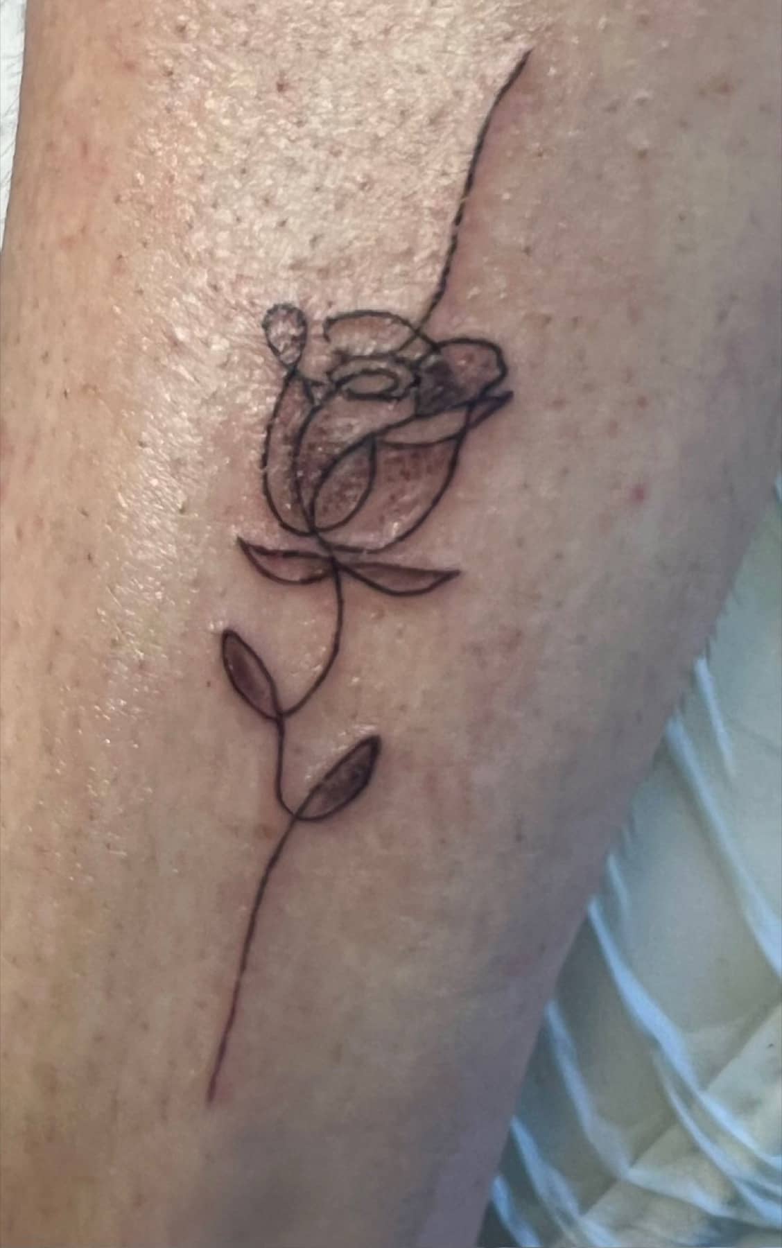 Single-line rose tattoo on the upper arm
